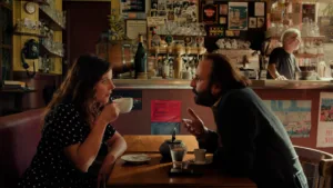 uma mulher está a beber café e um homem, à sua frente, fala com ela, estão num café