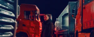 homem, de noite, entre três camiões, olha em frente