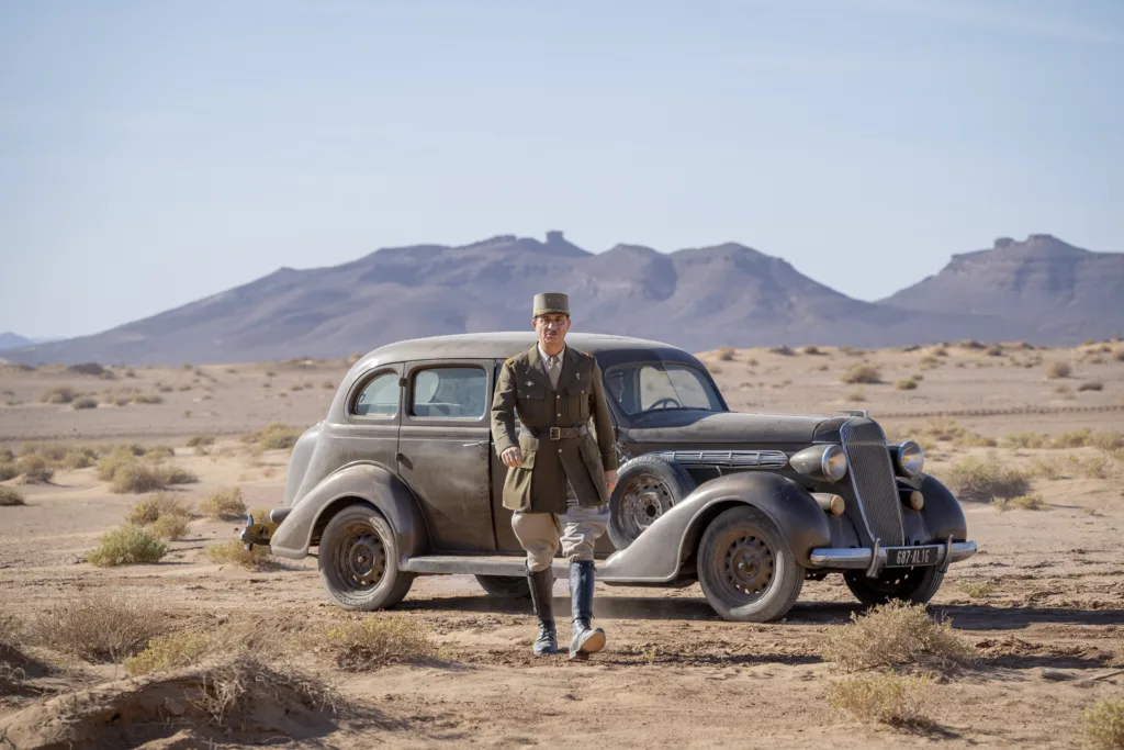 um carro antigo no meio do deserto e um general a andar em direção à câmara